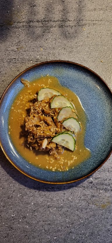 Gerecht met stukjes vlees, saus en schijfjes limoen op een blauwe schaal.